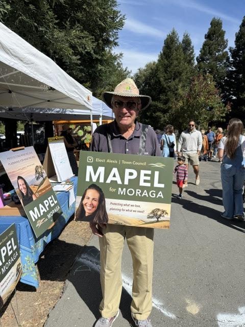 A supporter holding a Mapel for Moraga campaign sign at a community event
